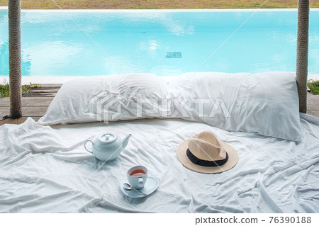 Traveler hat, hot tea cup and teapot on white bed against Beautiful ocean view background, Tourists relaxing in tropical resort with swimming pool. travel summer, vacation and freelance concept Traveler hat, hot tea cup and teapot on white bed against Beautiful ocean view background, Tourists relaxing in tropical resort with swimming pool. travel summer, vacation and freelance concept 76390188
