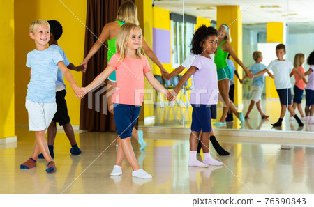 Happy kids and female teacher dancing together in studio at elementary school 76390843