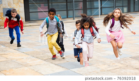 Happy tween schoolchildren with backpacks running to school outdoors Happy tween schoolchildren with backpacks running to school outdoors 76392018
