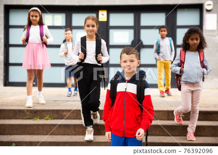 Positive boy standing near school, children on background Positive boy standing near school, children on background 76392096