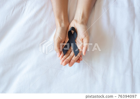 Melanoma and skin cancer, Vaccine injury awareness month and rest in peace concepts. Man holding black Ribbon on white bed background Melanoma and skin cancer, Vaccine injury awareness month and rest in peace concepts. Man holding black Ribbon on white bed background 76394097