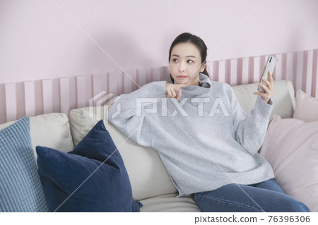 Asian woman using smart phone on couch 76396306