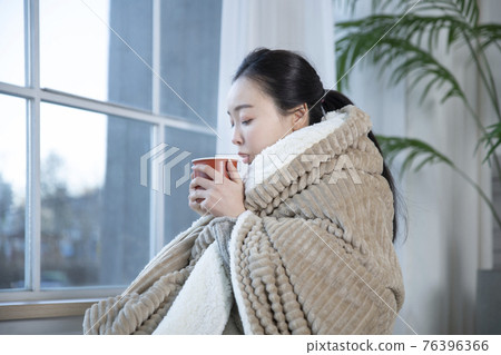 Asian woman drinking hot coffee or tea in blankets Asian woman drinking hot coffee or tea in blankets 76396366