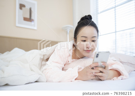 Asian woman waking up and checking smart phone Asian woman waking up and checking smart phone 76398215