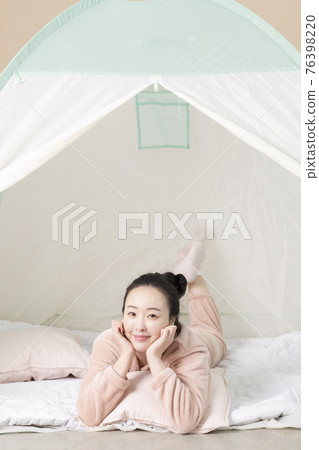 Asian woman in pajams under indoor bed tent Asian woman in pajams under indoor bed tent 76398220