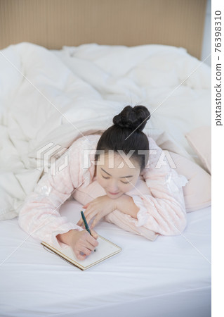 Asian woman writing planner, diary in bed 76398310