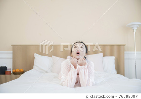 Asian woman with hair bun in pink pajamas on bed Asian woman with hair bun in pink pajamas on bed 76398397