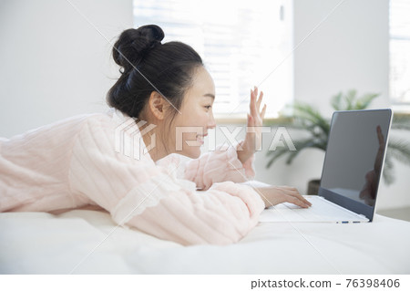 Asian woman in pajamas lying in bed using laptop, video chatting Asian woman in pajamas lying in bed using laptop, video chatting 76398406