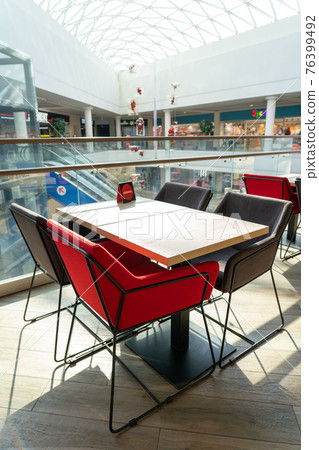A table and soft chairs for visitors to the food court of a modern shopping center. 76399492