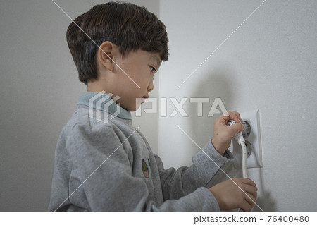 Asian boy inserting cords into an electrical outlet 76400480