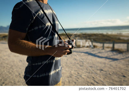 Midsection of caucasian man on the beach holding camera 76401702