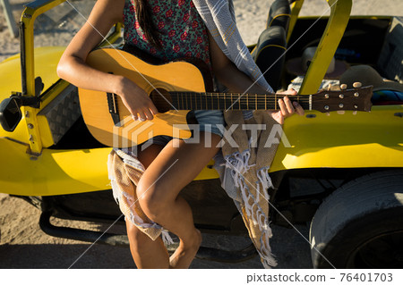Midsection of caucasian woman sitting on beach buggy by the sea playing guitar Midsection of caucasian woman sitting on beach buggy by the sea playing guitar 76401703