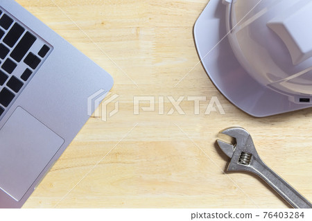 Close-up computer laptop, white security helmet and wrench put on wooden table with center copy space on top-view, technician engineering maintenance concept idea  76403284