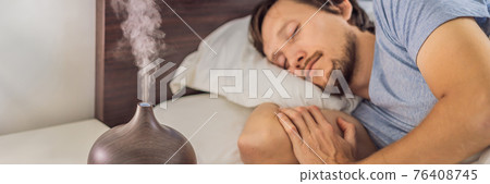 BANNER, LONG FORMAT Aromatherapy Concept. Wooden Electric Ultrasonic Essential Oil Aroma Diffuser and Humidifier. Ultrasonic aroma diffuser for home. Man resting at home 76408745