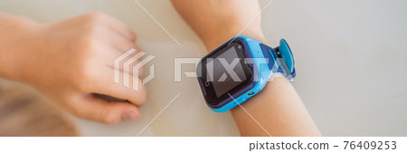 BANNER, LONG FORMAT Little boy sitting at the table and looking smart watch. Smart watch for baby safety. The child makes school lessons, listening to music, calling friends BANNER, LONG FORMAT Little boy sitting at the table and looking smart watch. Smart watch for baby safety. The child makes school lessons, listening to music, calling friends 76409253