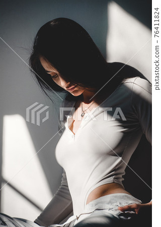 portrait of beautiful gentle woman in a white bodysuit posing in the sunshine. Black long hair. sensuality and tenderness portrait of beautiful gentle woman in a white bodysuit posing in the sunshine. Black long hair. sensuality and tenderness 76411824