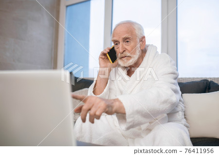 Gray-haired bearded man in white robe talking on the phone and looking busy Gray-haired bearded man in white robe talking on the phone and looking busy 76411956