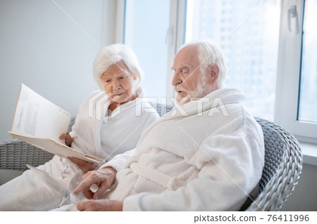 Senior couple in white robes choosing procedures in a spa center Senior couple in white robes choosing procedures in a spa center 76411996