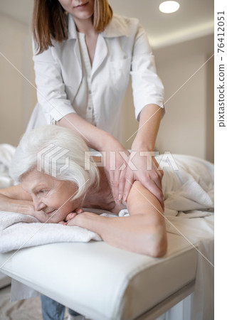 Massage therapist doing back massage to a senior female client 76412051