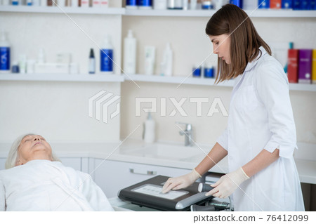 Cosmetologist in a white coat getting the apparatus ready for the procedures 76412099