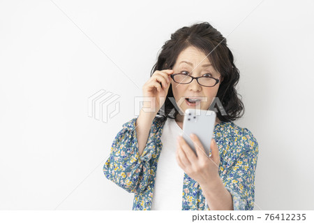 Senior woman wearing reading glasses and looking at her smartphone 76412235