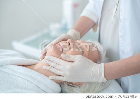 Mature woman enjoying face massage and looking relaxed Mature woman enjoying face massage and looking relaxed 76412499