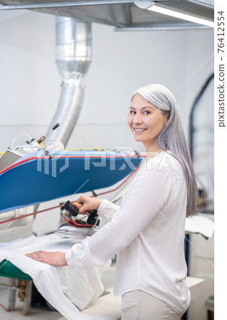 Woman with iron near counter at dry cleaning Woman with iron near counter at dry cleaning 76412554
