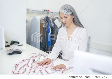 Woman looking at clothes lying on counter 76412579