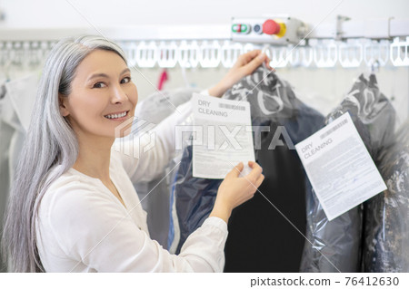Happy woman near clothes rack in dry cleaning Happy woman near clothes rack in dry cleaning 76412630