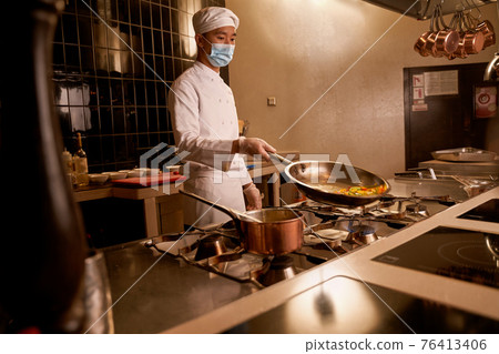 Asian cook tilting a hot pan with vegetable slices 76413406