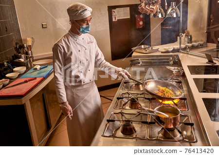 Asian kitchen worker frying vegetables on big flame 76413420