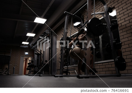 Fit woman squatting with barbell in gym 76416691