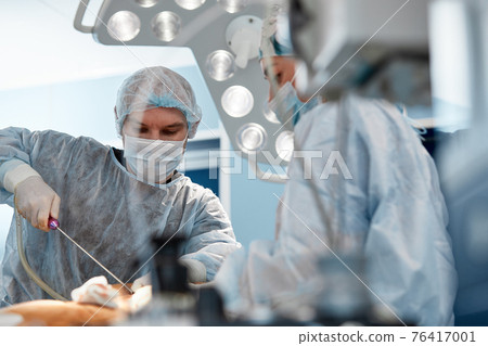 cosmetic liposuction surgery in actual operating room setting showing surgeon hands and cannula. 76417001