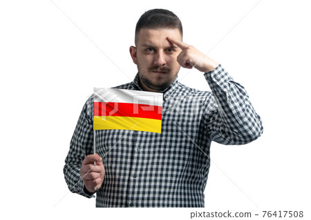 White guy holding a flag of South Ossetia and a finger touches the temple on the head isolated on a white background White guy holding a flag of South Ossetia and a finger touches the temple on the head isolated on a white background 76417508