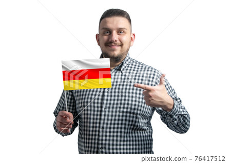 White guy holding a flag of South Ossetia and points the finger of the other hand at the flag isolated on a white background White guy holding a flag of South Ossetia and points the finger of the other hand at the flag isolated on a white background 76417512