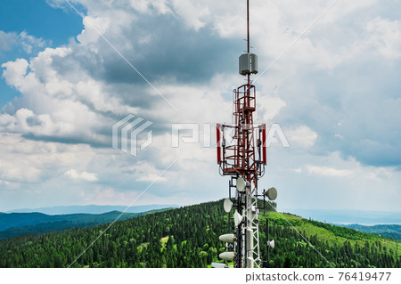 Telecommunication transmitter tower with antennas of cellular communication in mountains against sky and clouds 76419477