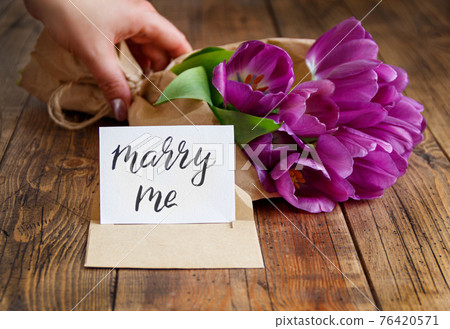 Hand with Bouquet and MARRY ME card on wooden table 76420571