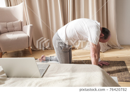 Senior man working out at home in living room, doing yoga exercise on mat. Senior man working out at home in living room, doing yoga exercise on mat. 76420782