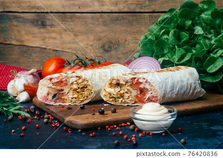 Doner kebab (shawarma or doner wrap). Grilled chicken on lavash (pita bread) with fresh vegetables - tomatoes, green salad, peppers. Old wooden background. Middle Eastern food, arabic fast food 76420836