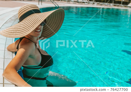 Summer hat pool. Young sexy woman in straw hat, bikini swimsuit, sunglasses swimming in blue water. Luxury lifestyle travel. Summer hat pool. Young sexy woman in straw hat, bikini swimsuit, sunglasses swimming in blue water. Luxury lifestyle travel. 76427700
