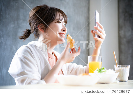 年輕女子在吃早餐時使用智能手機 76429677