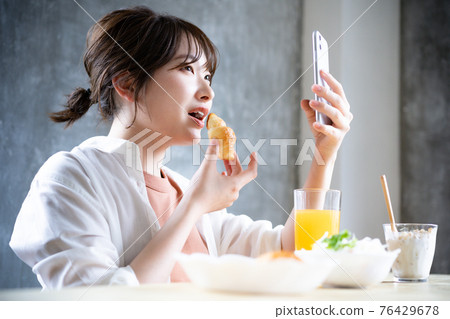年輕女子在吃早餐時使用智能手機 年輕女子在吃早餐時使用智能手機 76429678