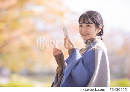 A woman using a smartphone in an autumn park 76430935