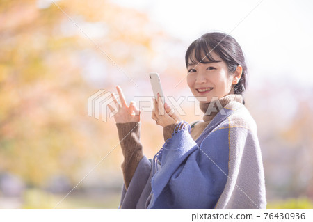 A woman using a smartphone in an autumn park 76430936