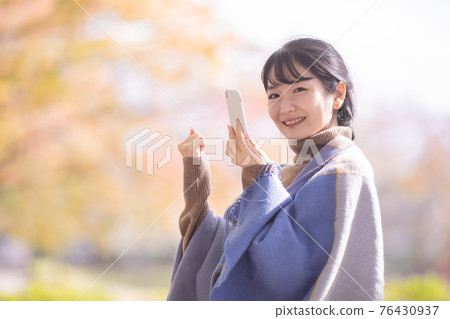 A woman using a smartphone in an autumn park A woman using a smartphone in an autumn park 76430937