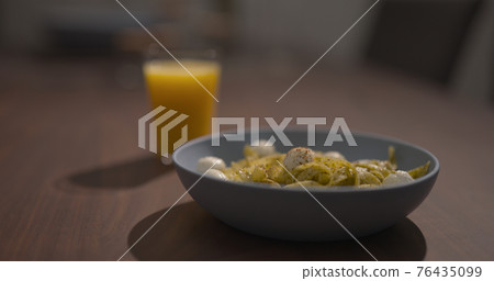 blue bowl with pesto fettuccine on walnut table with orange juice 76435099