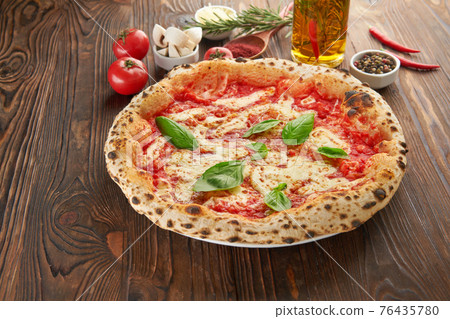 Original italian neapolitan pizza Margherita with melted mozzarella cheese, fresh basil leaves and tomato sauce on wooden table with ingredients. Fast food italian menu and vegetarian eating concept Original italian neapolitan pizza Margherita with melted mozzarella cheese, fresh basil leaves and tomato sauce on wooden table with ingredients. Fast food italian menu and vegetarian eating concept 76435780