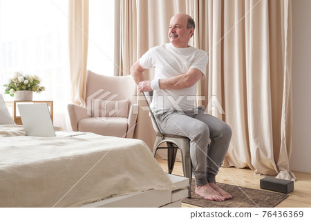 Sporty senior man practicing yoga using chair, doing Parivrtta Utkatasana 76436369