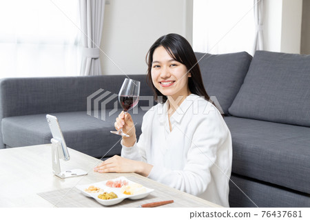 Young woman having an online drinking party on her smartphone Young woman having an online drinking party on her smartphone 76437681