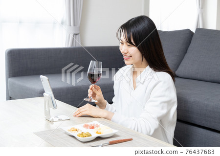 Young woman having an online drinking party on her smartphone 76437683